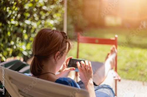 Lazy day at home. Sitting girl is enjoying the day on the porch, using her smartphone © Patrick Daxenbichler
