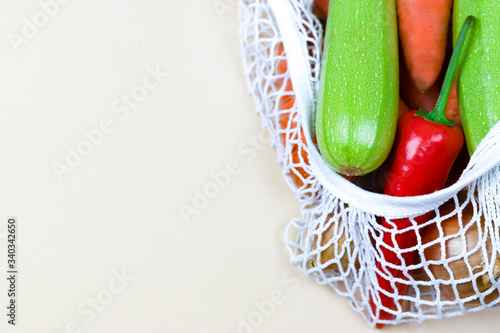 colored vegetables in a koton string shopping bag on a neutral beige background. eco zero waste concept. no plastic photo