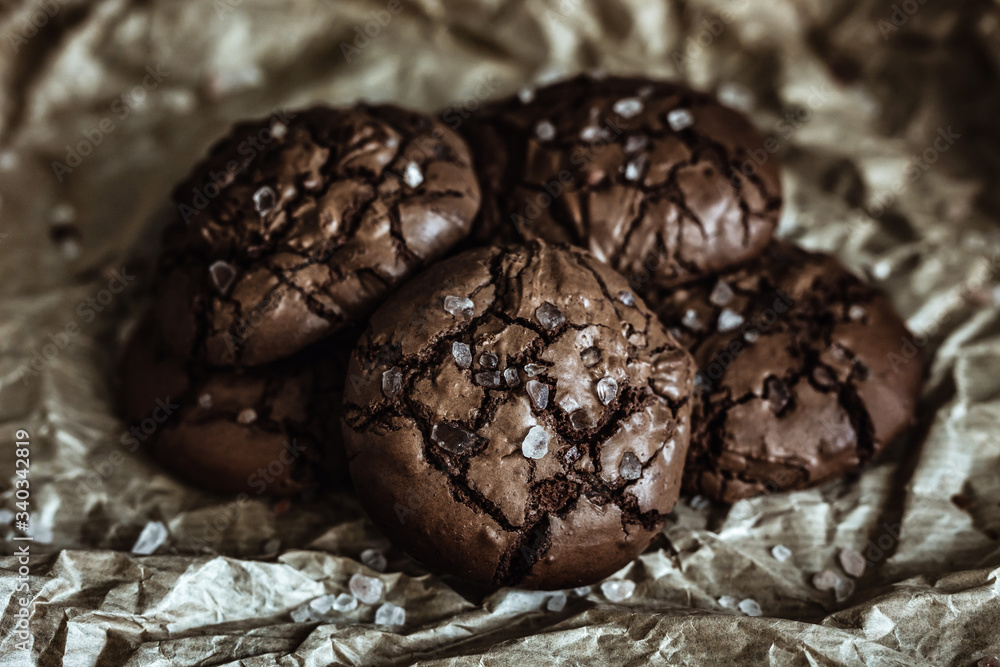 A pile of chocolate cookies with cracked tops with sea salt on craft paper A pile of chocolate cookies with cracked tops with sea salt on craft paper