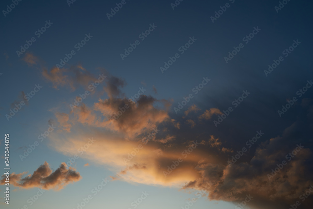 Obraz premium Beautiful evening blue sky at sunset with flaming bright light clouds. A warm summer evening.