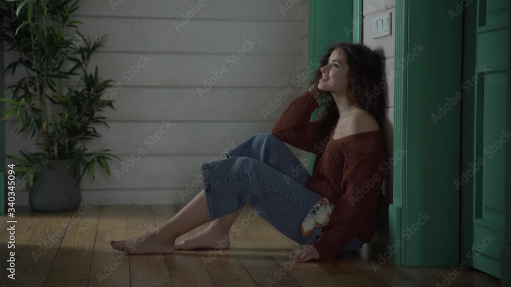 a beautiful young girl with curly hair in jeans and a brown cardigan sitting on the floor looks thoughtfully at vrekh then laughs. a beautiful young girl with curly hair in jeans and a brown cardigan sitting on the floor looks thoughtfully at vrekh then laughs.