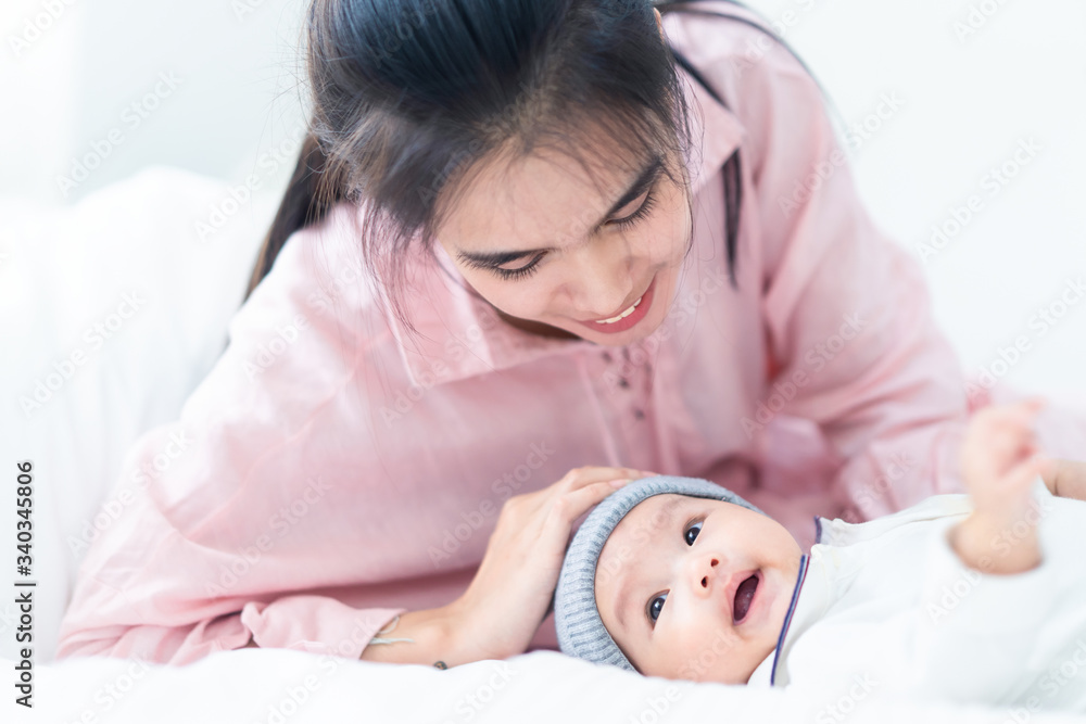 Close up view of beautiful Asian mother and her cheerful lovely newborn baby. Mother holding baby head in one hand and put her head near the kid talking with infant and smiling. Happy family concept. Close up view of beautiful Asian mother and her cheerful lovely newborn baby. Mother holding baby head in one hand and put her head near the kid talking with infant and smiling. Happy family concept.