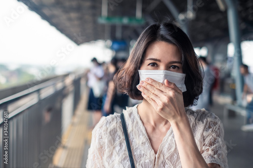 Asian woman wearing face mask for prevent dusk pm 2.5 bad air pollution and coronavirus or covid19 having a dry cough. Girl avoiding smell and protect virus infection from people at train station.