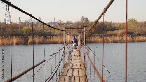 Petrovo, Dnipro / Ukraine - April 15 2020
Old suspension bridge over the river. Wooden bridge on steel cables. Village bridge. photo