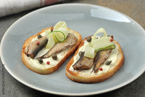 Two sandwiches with sprats, slices of fresh cucumber and capers.  Sandwiches occupy the entire space of the frame.  Light background.  Close-up.