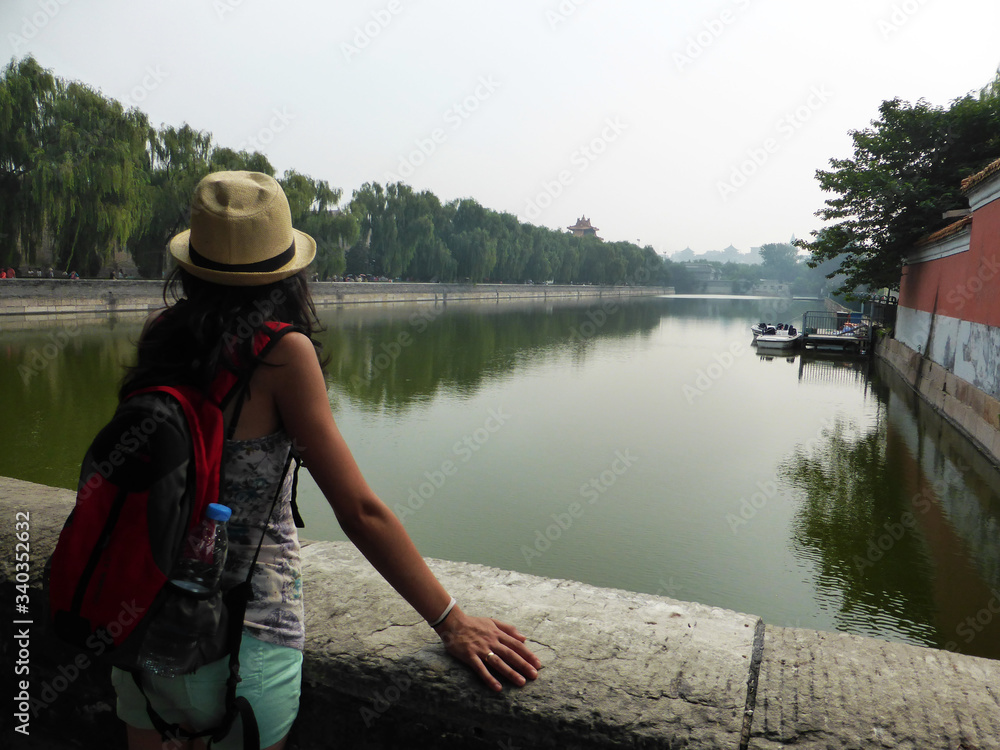 Viajera con gorro y mochila mirando el muro y foso de la Ciudad Prohibida en Beijing, China. Viajera con gorro y mochila mirando el muro y foso de la Ciudad Prohibida en Beijing, China.