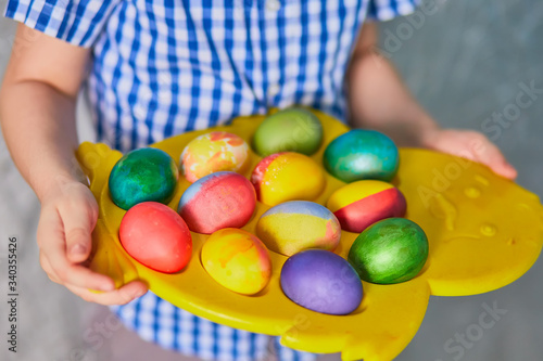 little boy with no face visible holding basket full of colorful easter eggs standing on the grass in the park after egg hunt