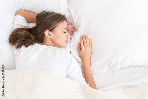 Young female spending late morning in bed, sleeping peacefully on white linen, concept of calm and serene dream, copy space on right