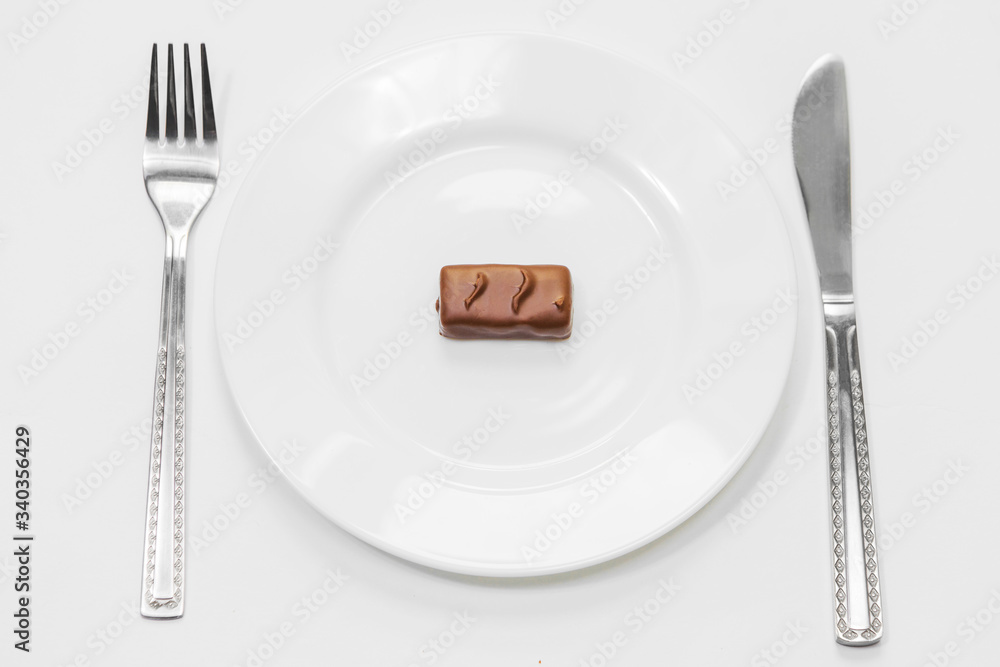 Chocolate bars on white plate with fork and knife on white background. Unhealthy high-calorie diet Chocolate bars on white plate with fork and knife on white background. Unhealthy high-calorie diet