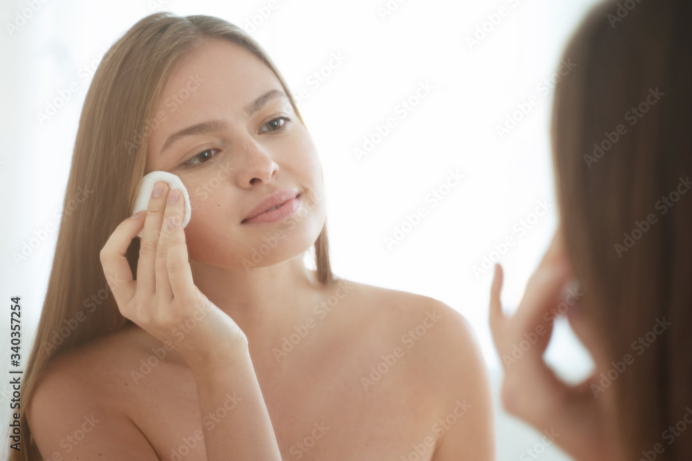 Girl in bathroom, cleaning her skin with cotton pad with lotion, taking care of her facial state, enjoying beauty rituals in morning Girl in bathroom, cleaning her skin with cotton pad with lotion, taking care of her facial state, enjoying beauty rituals in morning