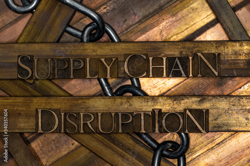 Photo of real authentic typeset letters forming Supply Chain Disruption text with steel chain on vintage textured grunge copper and gold background