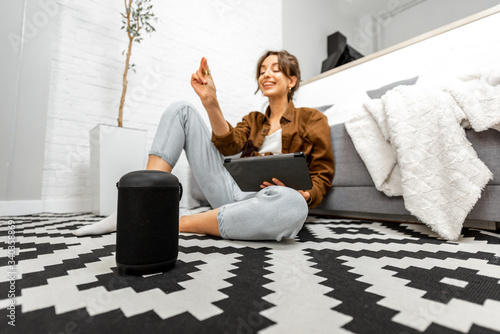 Woman using voice commands to control a smart home devices sitting with a smart speaker and tablet on the floor in the living room photo