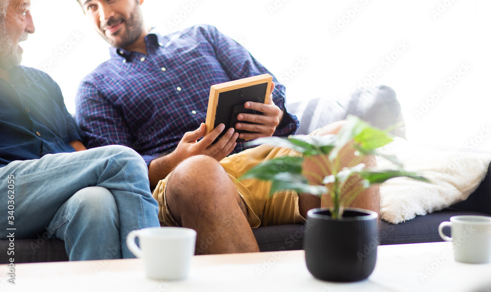 Father and son family time together at home concept. Happy old father and son sitting together and looking photos while remembering old times past. Father and son family time together at home concept. Happy old father and son sitting together and looking photos while remembering old times past.