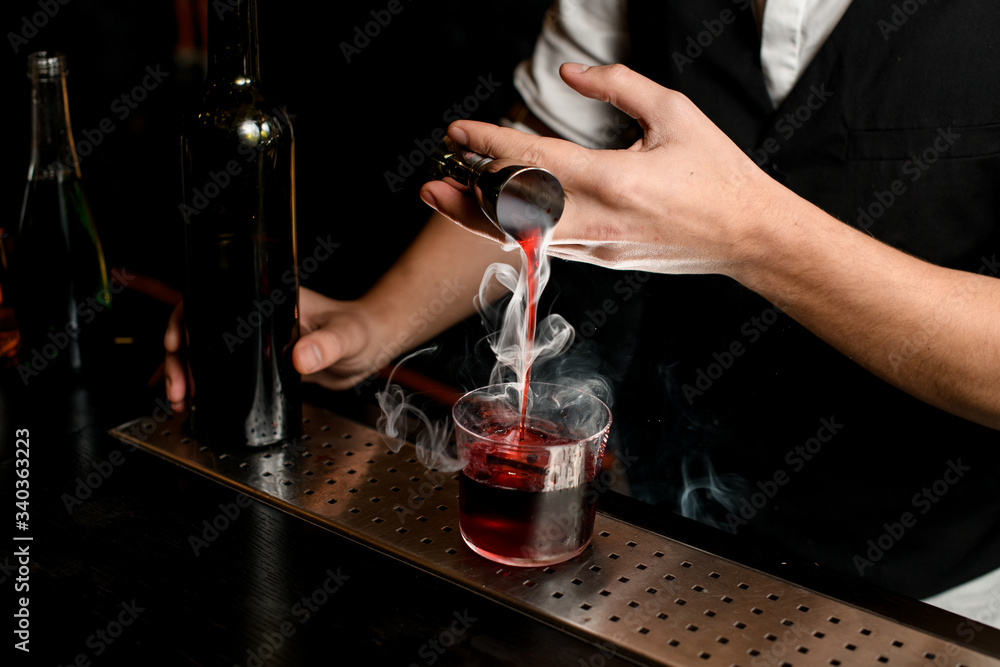 close-up. Bartender's hand masterfully pours smoky drink from jigger into glass with ice