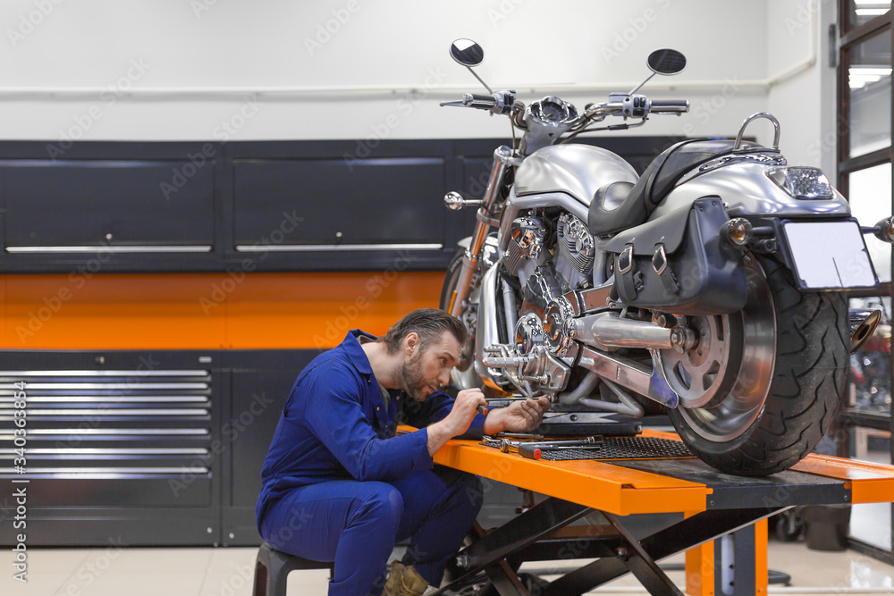 custom made wallpaper toronto digitalMan fixing a motorcycle raised on a lift in a modern workshop.