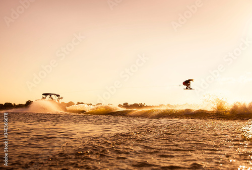 A woman wakeboarder getting some air behind the boat at sunset