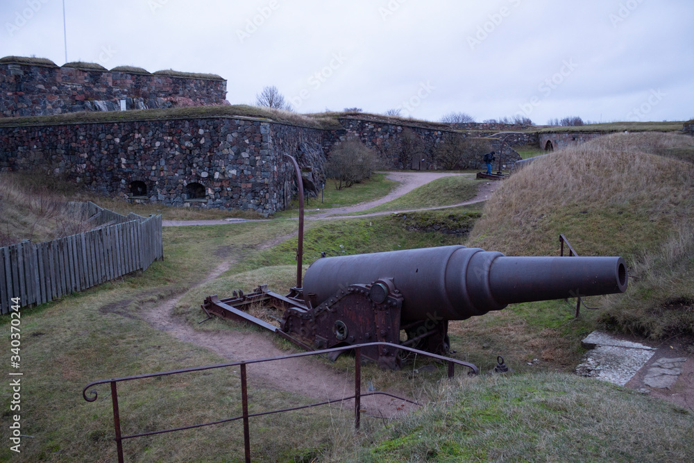 On an autumn day in Finland, an old cast-iron artillery gun and old granite fortifications on the island of Fort Suomenlinna were overgrown with grass.