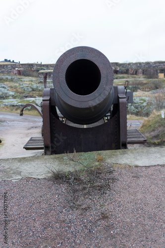 The barrel of a large cast-iron old cannon from the time of the Russian Empire against the background of the old fortifications of the historical fort Suomenlinna, in Helsinki, Finland, autumn