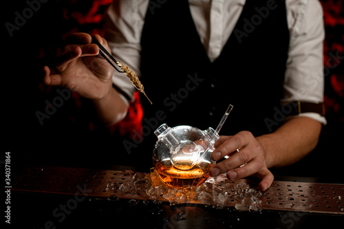 close-up male bartender decorate with spikelet designer flask with alcoholic drink