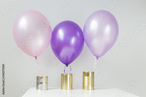 Concept. Three tin cans on a white table. Each tin has a balloon. Pink and purple. Volunteering. Food denation. Helping the needy. Gold, silver.