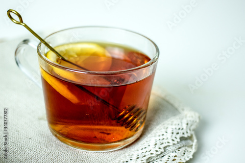 A transparent mug with black tea, a slice of lemon, a spoon for honey on a wicker gray napkin on a light table. The concept of a cozy tea party. Close-up