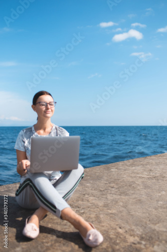 Beautiful young woman sitting with a laptop by the sea. Webinar online teaching concept. Online work.