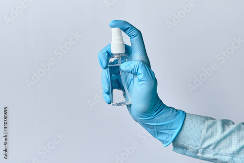 Doctor in a dressing gown and medical gloves spray an antiseptic sanitizer on a white background.