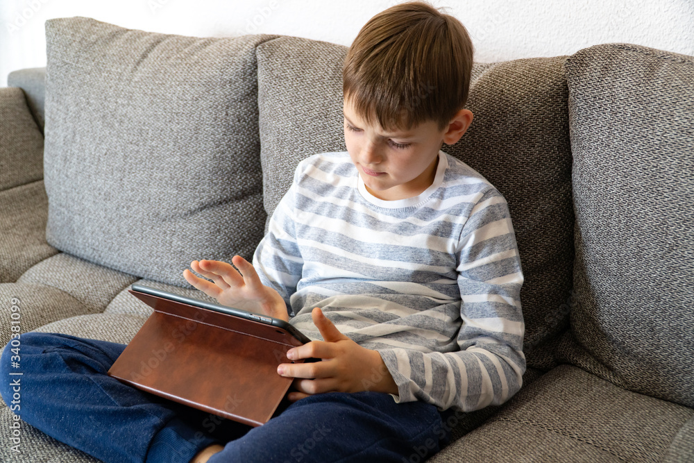 Looking up young boy thinking in front of tablet pc. Distance learning online education. Cute caucasian boy doing homework at home while quarantine of pandemia coronavirus. Looking up young boy thinking in front of tablet pc. Distance learning online education. Cute caucasian boy doing homework at home while quarantine of pandemia coronavirus.