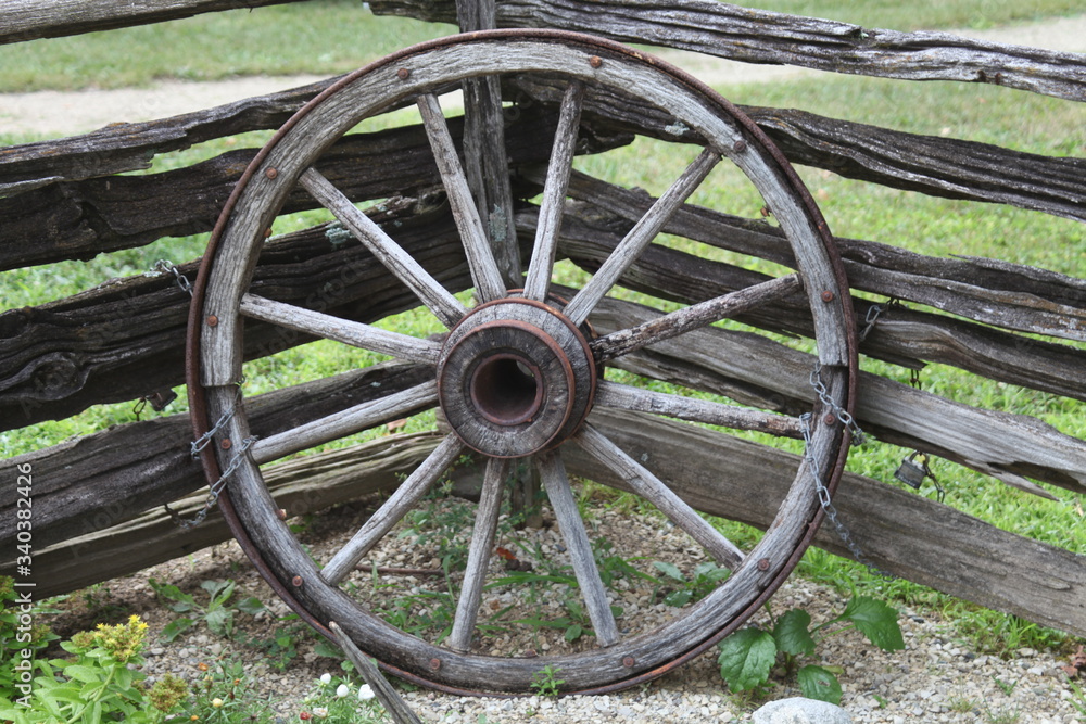 WOOD WHEEL, SHAPE, WAGON, RUSTIC IN COLOR, NEXT TO A OLD FENCE WOOD WHEEL, SHAPE, WAGON, RUSTIC IN COLOR, NEXT TO A OLD FENCE