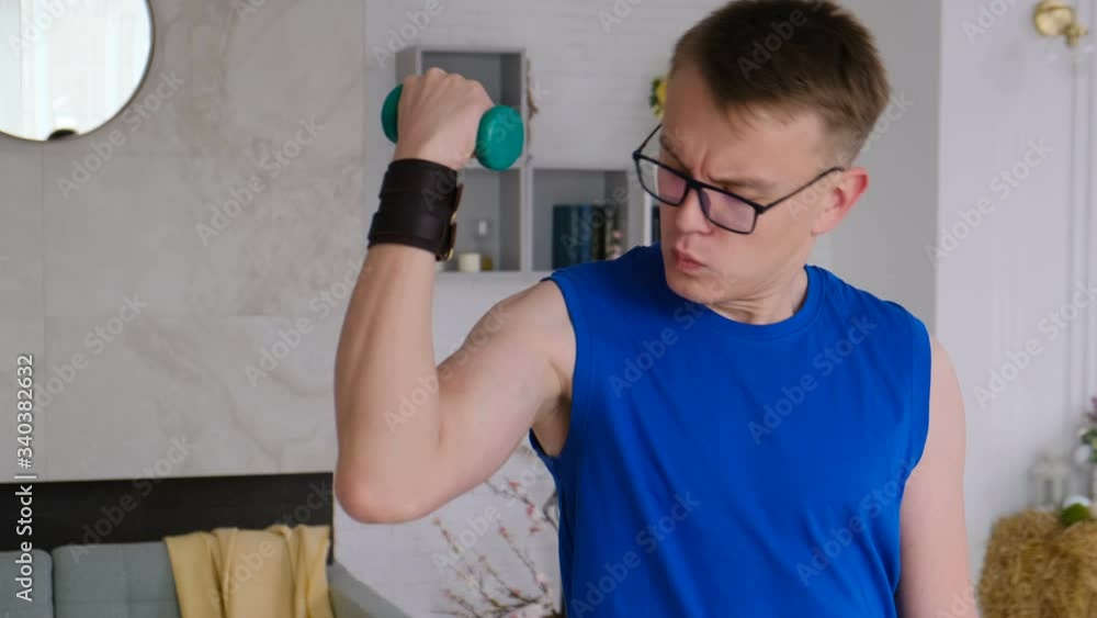 Funny guy shaking his little dumbbell's biceps and looking at him at home. The guy dreams of a big biceps muscle Funny guy shaking his little dumbbell's biceps and looking at him at home. The guy dreams of a big biceps muscle