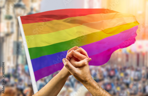  couple holding hands and wave in front of a rainbow flag