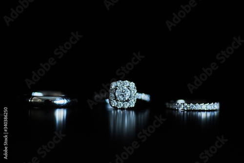 Engagement ring, and two weddings bands along a dark surface with a dark background.