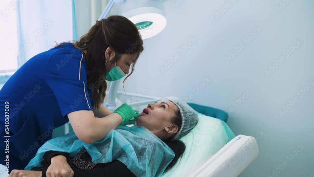 female cosmetology doctor in blue uniform and mask does injection for augmentation into mature woman lower lip in professional beauty clinic female cosmetology doctor in blue uniform and mask does injection for augmentation into mature woman lower lip in professional beauty clinic