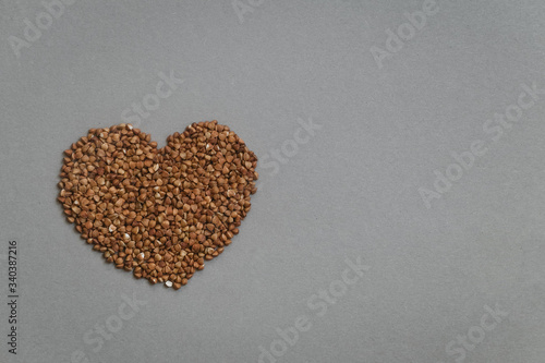 Heart-shaped uncooked buckwheat on the grey background. Healthy diet, copy space.