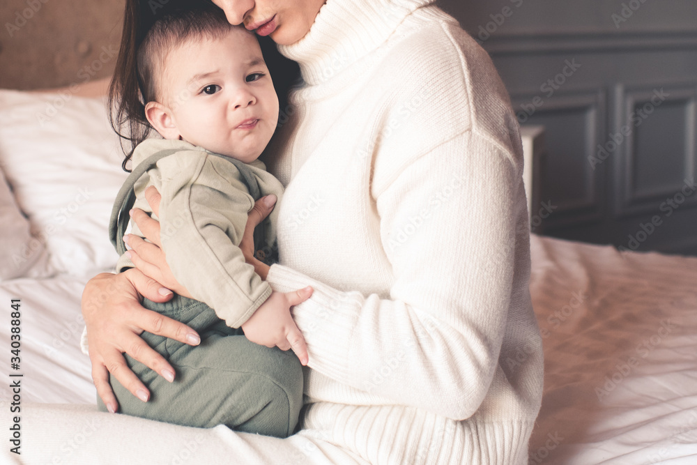 Crying baby boy sitting on mother hands in bed closeup. Looking at camera. Motherhood. Maternity. Crying baby boy sitting on mother hands in bed closeup. Looking at camera. Motherhood. Maternity.