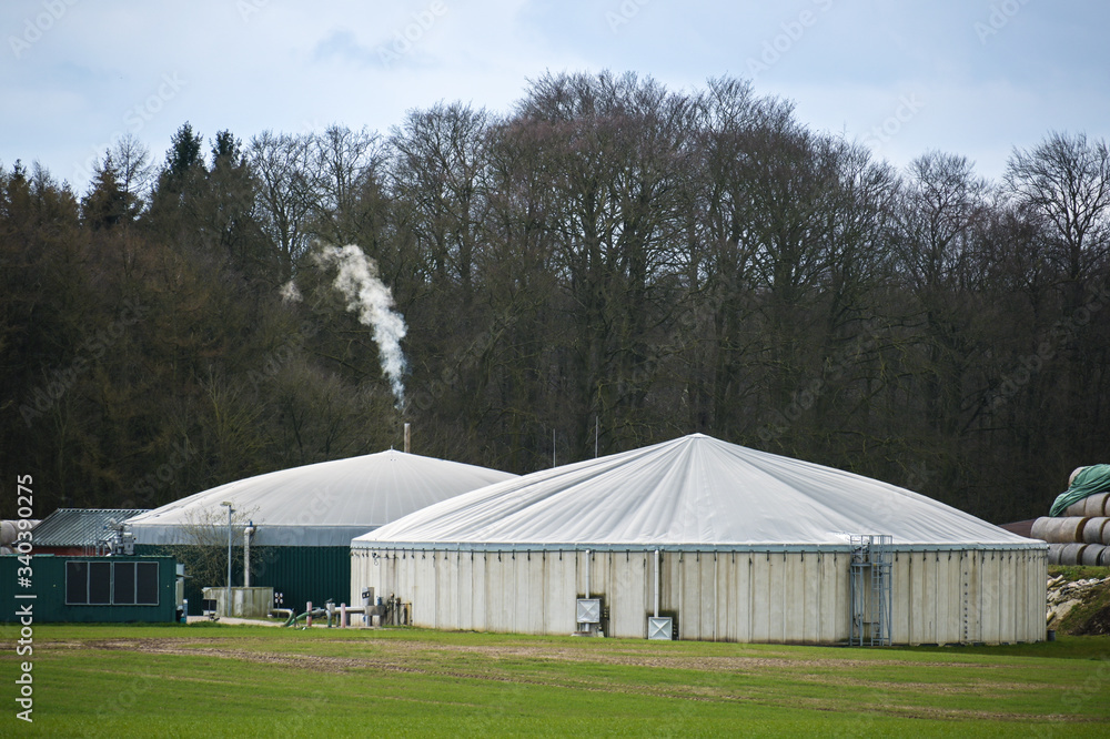 Biogas plant with smoking chimney at the edge of a  forest, cloudy sky, copy space