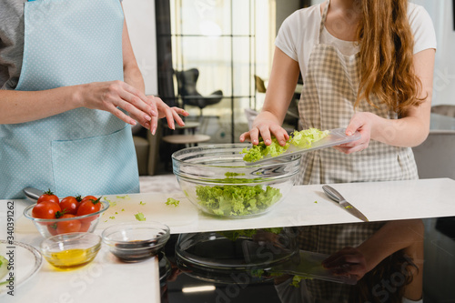 Women put green salad at bowl indoors
