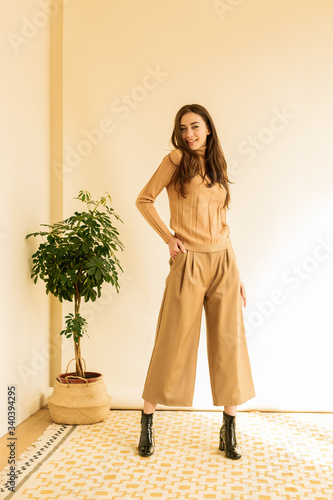 Fashion portrait of young happy smiling lady wearing trendy beige turtleneck, high-waisted checkered trousers