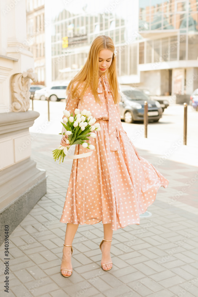 Outdoor portrait of a beautiful young blonde woman. Attractive girl on the street with flowers. Smiling happy girl in dress Outdoor portrait of a beautiful young blonde woman. Attractive girl on the street with flowers. Smiling happy girl in dress