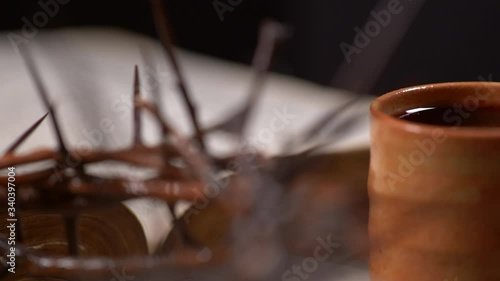 Cup filled with wine with Crown of Thorns and old Bible panning right