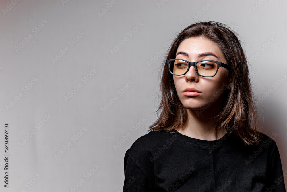 young brunette woman looking away in glasses and a black t-shirt on a gray background
