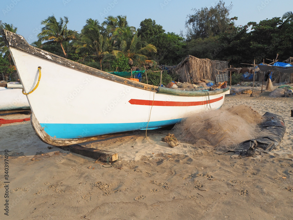 An old wooden fishing boat stands on the shore in India. nearby are nets for fishing