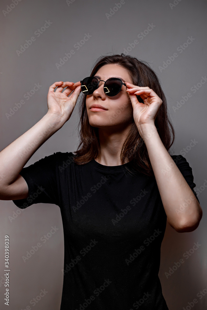 young brunette woman in black sunglasses and a black t-shirt on a gray background young brunette woman in black sunglasses and a black t-shirt on a gray background