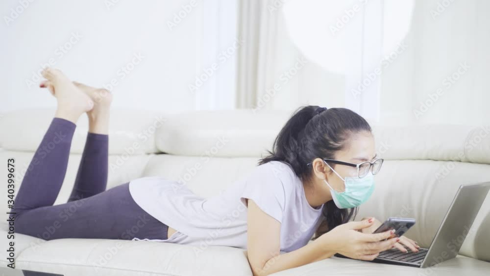 Work from home concept. Young woman lying on the couch while using a cellphone and computer laptop during quarantine at home. Shot in 4k resolution Work from home concept. Young woman lying on the couch while using a cellphone and computer laptop during quarantine at home. Shot in 4k resolution
