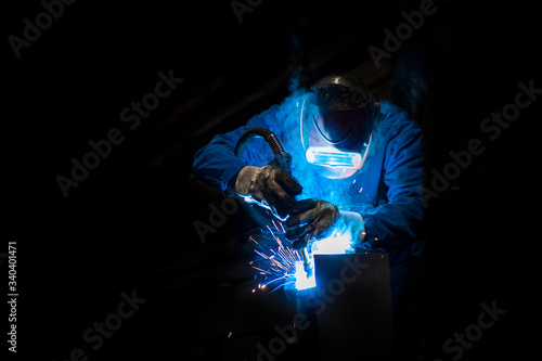 Man welding in a fabric with sparks, dark background