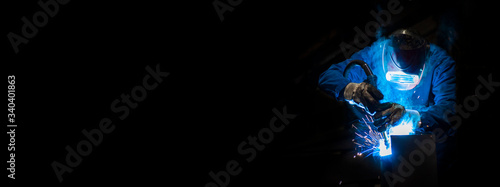 Man welding in a fabric with sparks, dark background