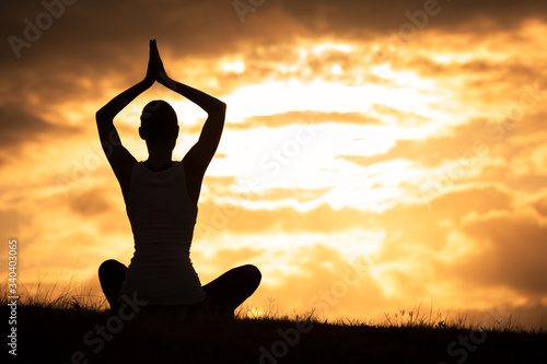 silhouette of a woman doing yoga on sunset on a grass field. 