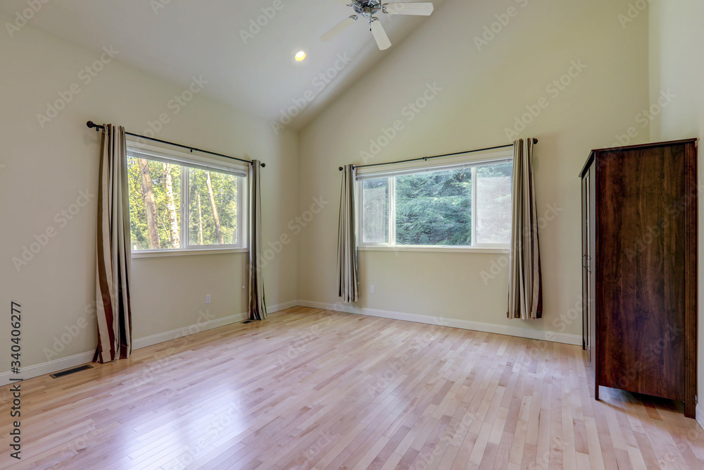 Empty bedroom interior with grey curtains and tall vaulted ceiling - with dark wooden dresser. Empty bedroom interior with grey curtains and tall vaulted ceiling - with dark wooden dresser.