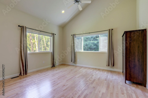 Empty bedroom interior with grey curtains and tall vaulted ceiling - with dark wooden dresser.