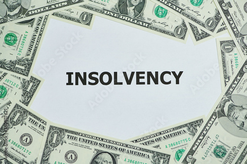word insolvency printed on a white paper, around are lying Dollar bills